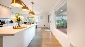 Une cuisine moderne dotée d’un îlot central, de luminaires suspendus et offrant une vue sur l’extérieur.