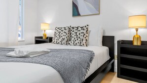 Ein Hotelzimmer mit einem Bett, zwei Nachttischen mit Lampen, einem Bild an der Wand und einem Fenster mit Vorhängen.