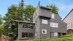 A modern two-story house with a stone foundation, large windows, and a wooden fence. - 9852 Upper · 4b2b Upper Unit @S Seattle w/ Panoramic Lake View (Seattle)