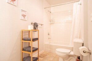 A bathroom with a shower, toilet, and a wooden shelf with towels.
