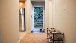 A narrow hallway with a kitchen area on the left, a shoe rack on the right, and a door leading to a garden. - 9852 Upper · 4b2b Upper Unit @S Seattle w/ Panoramic Lake View (Seattle)