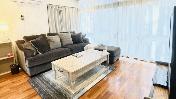 A modern living room with a grey sofa, a wooden coffee table, and a TV stand. - Chatan Beach House 1 (Chatan)