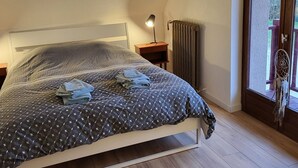 Ein Schlafzimmer mit einem Bett, einer Nachttischlampe, einer Heizung und einem Fenster mit Blick auf Bäume.