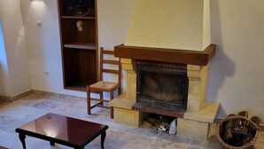 Ein Wohnzimmer mit Kamin, einem Holzstuhl, einem kleinen Tisch und einem Korb.