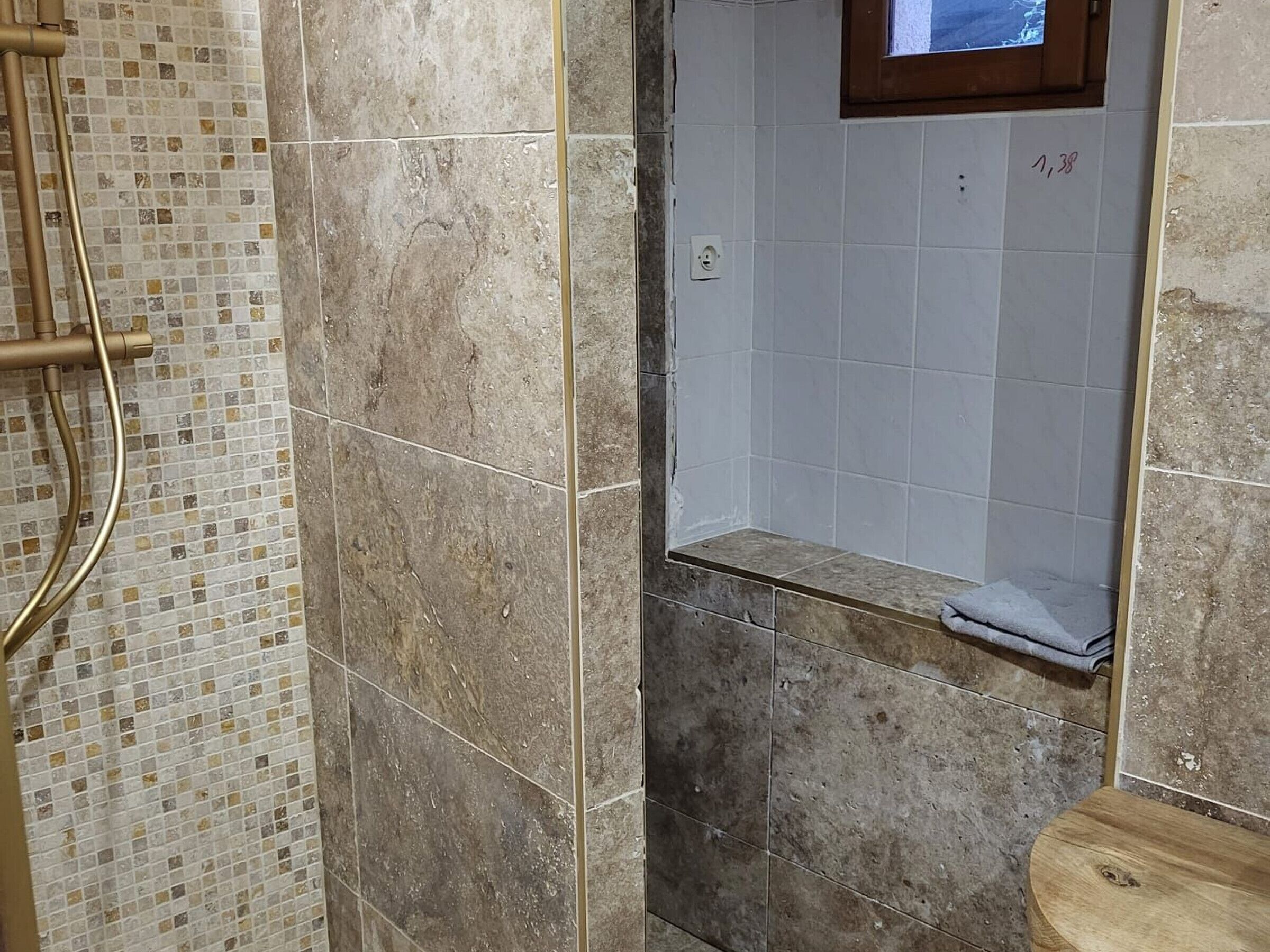 A bathroom with a shower area, tiled walls, and a wooden bench.