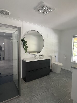 A modern bathroom with a glass shower enclosure, a round mirror, a dark vanity, and a toilet.