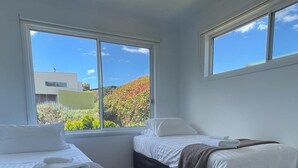 Une chambre avec deux lits, un tapis blanc et de grandes fenêtres donnant sur un paysage verdoyant et un immeuble.