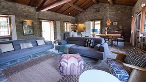 A spacious living area with a stone wall, a wooden ceiling, and a large sofa set. - Charming & Authentic Stone House La Brugna (Baselica, frazione di Borgo Val Di Taro)
