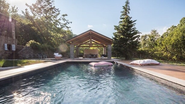 A swimming pool with a wooden gazebo, surrounded by trees and a stone building. - Charming & Authentic Stone House La Brugna (Baselica, frazione di Borgo Val Di Taro)
