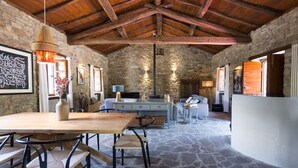 A rustic interior with stone walls, a wooden ceiling, a dining area with a table and chairs, a sofa, and a white counter. - Charming & Authentic Stone House La Brugna (Baselica, frazione di Borgo Val Di Taro)