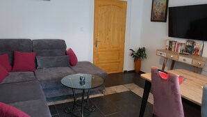 A living room with a grey sofa, red cushions, a glass coffee table, a wooden door, a flat-screen TV, and a desk with books and a plant. - Year-round holiday home with swimming pool and whirlpool. Dogs welcome! (Döbrököz)