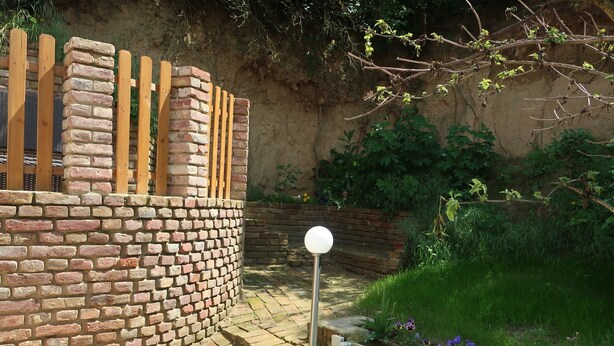 A brick wall with a wooden fence, a spherical light post, and a garden with various plants and flowers. - Year-round holiday home with swimming pool and whirlpool. Dogs welcome! (Döbrököz)