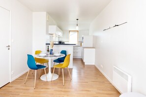 A modern kitchen with white cabinets, a dining area with a round table and colorful chairs, and a visible window with natural light.