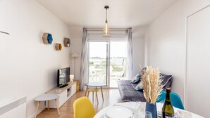 Un salon moderne comprenant un coin repas, un téléviseur et une vue à travers la porte vitrée.