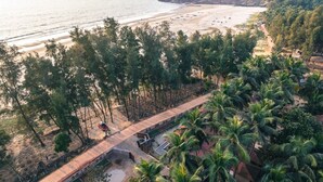 Vista costera con playa, palmeras y un paseo de madera que lleva a un edificio.