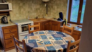 Une cuisine compacte équipée d’un four à micro-ondes, d’une cuisinière et d’un évier. On y trouve une table ronde recouverte d’une nappe à motifs et des chaises en bois.