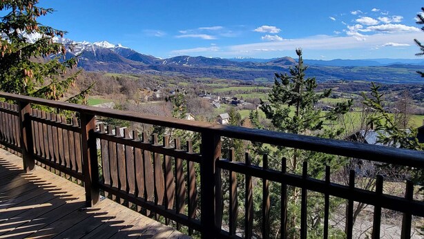 Eine Holzdar Terrasse mit Blick auf eine gebirgige Landschaft und ein Dorf darunter.
