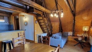 Ein gemütlicher Loftsraum mit Esstisch aus Holz, Stühlen, einer Couch und einer Treppe.