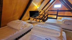 Ein gemütliches Dachzimmer mit drei Betten, einem Fernseher und einer Holztreppe.