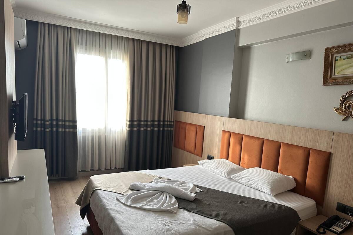 A hotel room with a large bed, a bedside table with a phone, and a window with curtains.