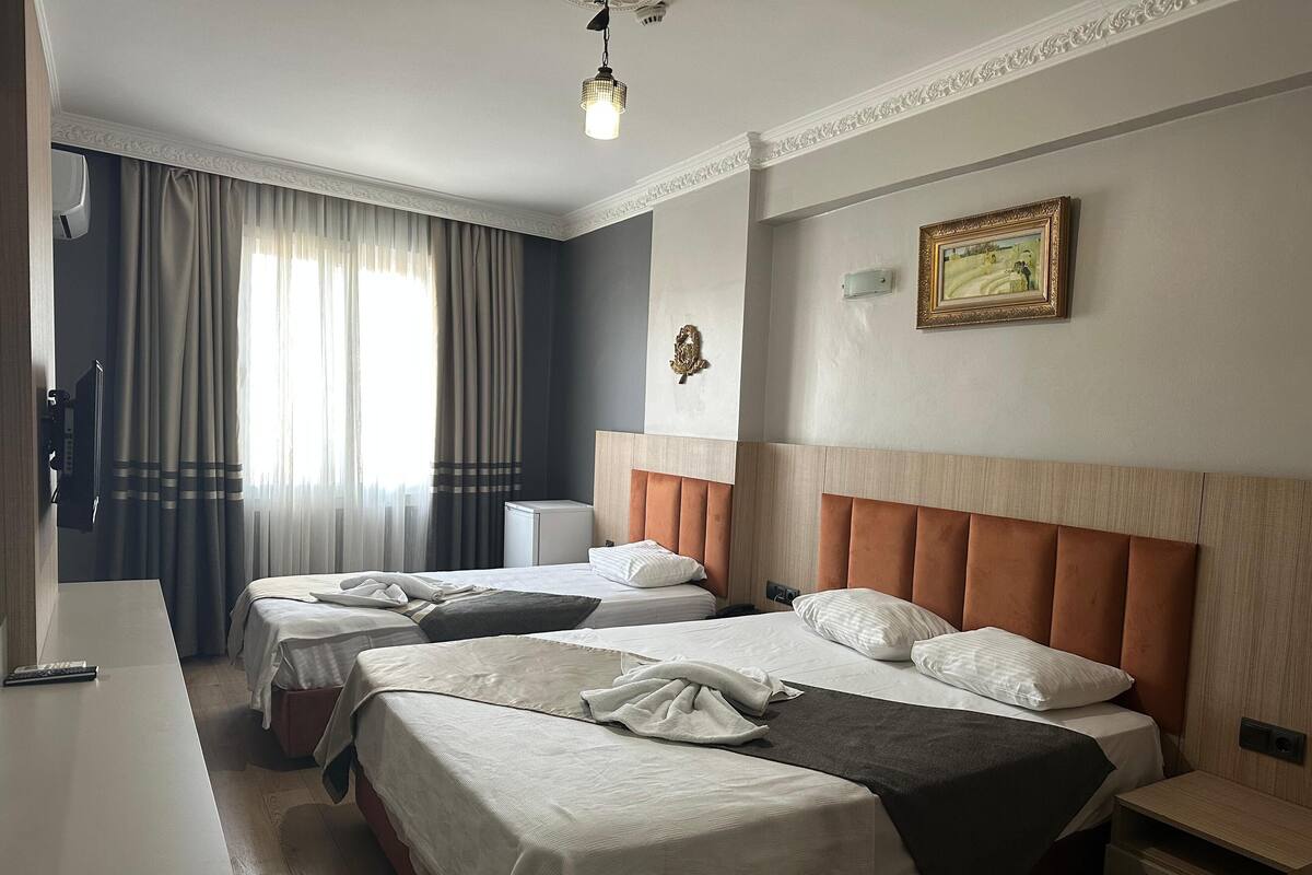 A hotel room with two beds, a desk, a chair, a nightstand, a lamp, and a painting on the wall.