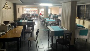 A spacious dining area with multiple tables and chairs, a tiled floor, and a view of the street through large windows. - Metros Hotel (Mersin)