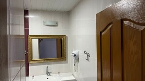 A bathroom with a white sink, a mirror with a gold frame, a hairdryer, and a wooden door. - Metros Hotel (Mersin)