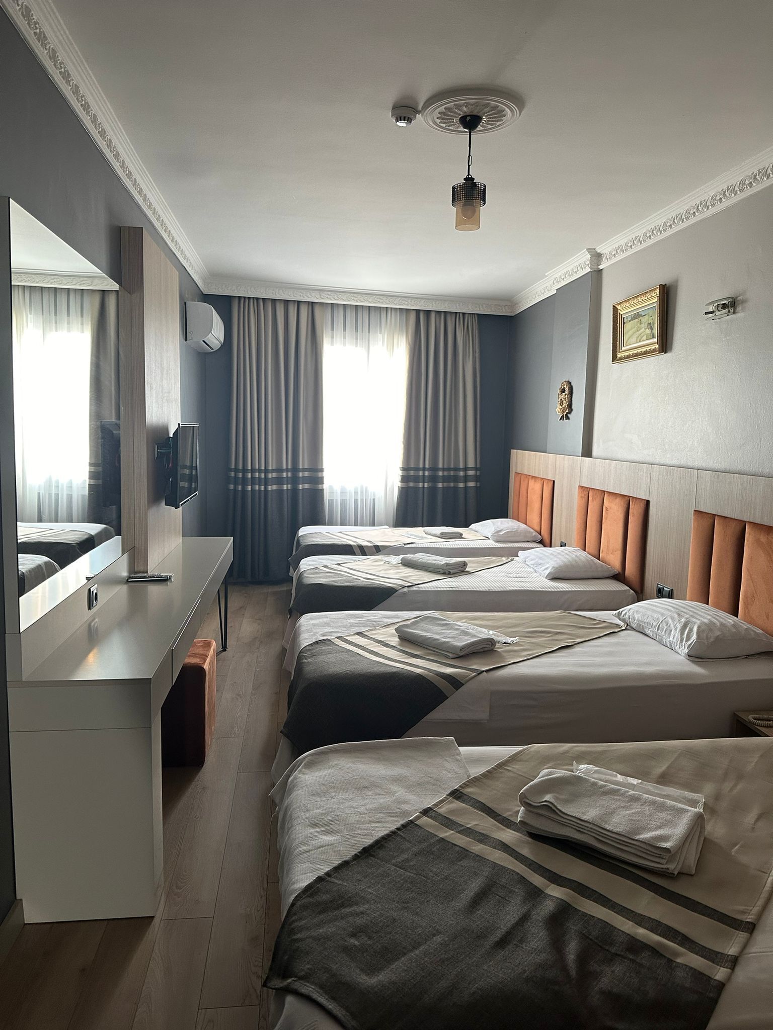 Habitación de hotel con tres camas, un escritorio, un espejo y un ventilador de techo.