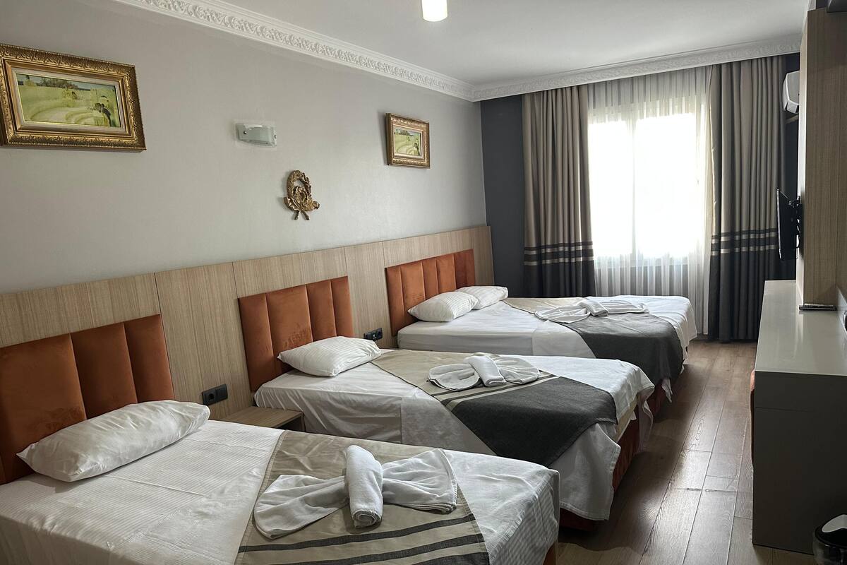 A hotel room with three beds, a desk, and a large window with curtains.