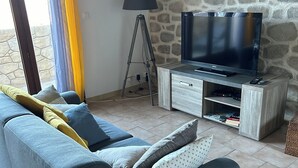 Un salon avec un canapé, un téléviseur posé sur un meuble en bois, une lampe et un mur en pierre.