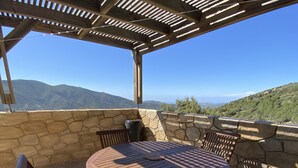 Une terrasse couverte avec une table ronde et des chaises, des murs en pierre et une vue sur les montagnes lointaines.