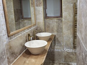 Un baño con dos lavamanos grandes y redondos, un mueble de tocador de madera y una cabina de ducha con paredes de vidrio.