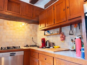 Een keuken met houten kastjes, een gasfornuis, een vaatwasser en diverse keukengerei.