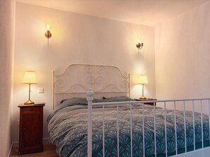 Een slaapkamer met een metalen hoofdbord, twee bedlampen, een houten nachtkastje en een bed met beddengoed met een patroon.