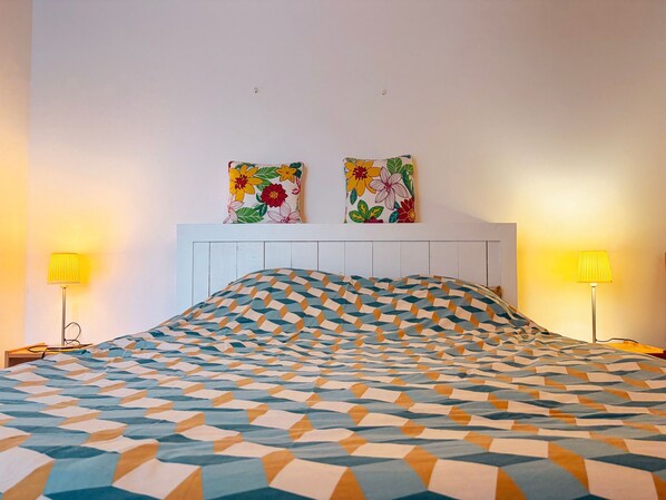 Een hotelkamer met een bed met een patroon, twee aan de muur bevestigde schilderijen en twee bedlampen.