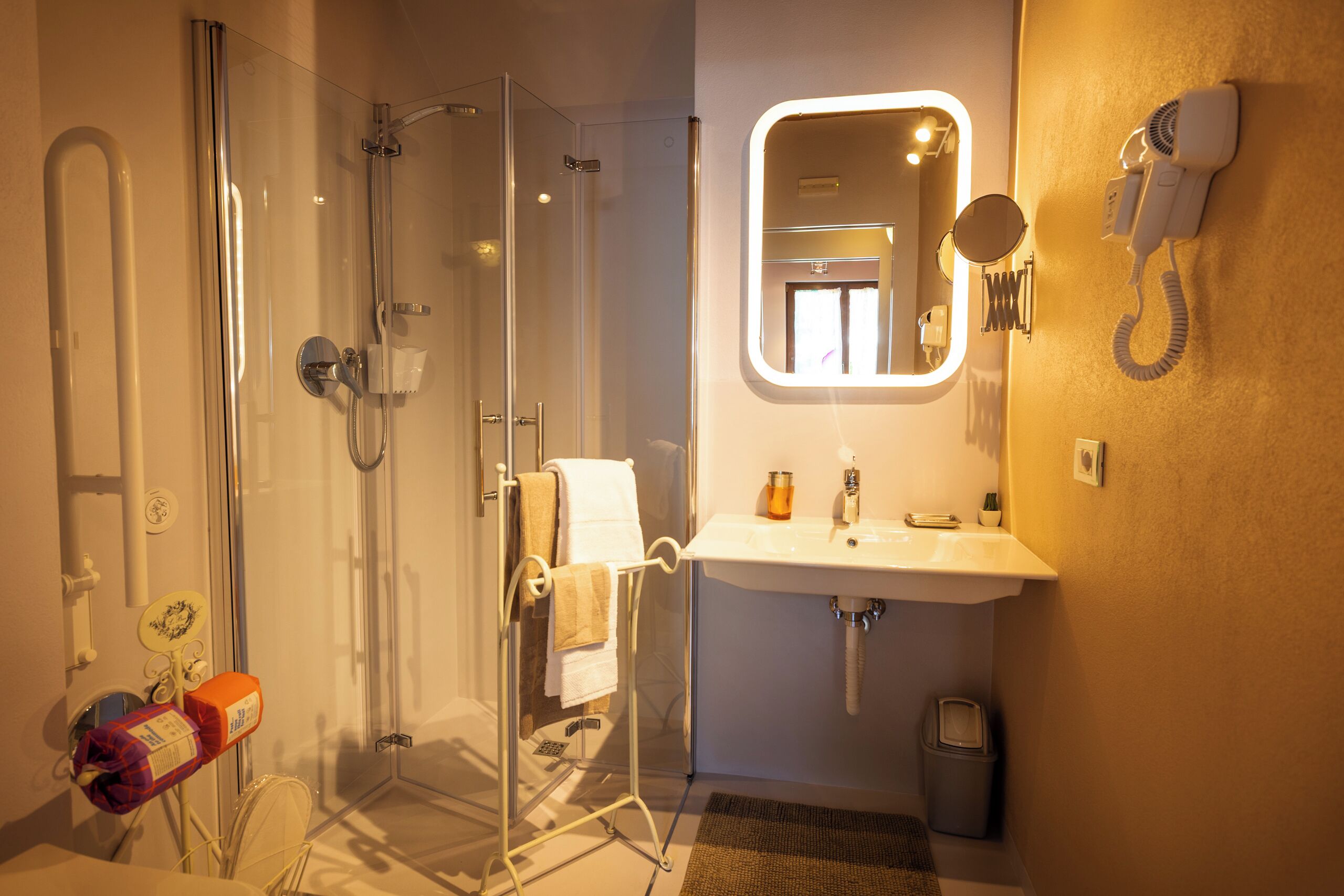 A modern bathroom with a glass-enclosed shower, a sink with a mirror, and a hairdryer mounted on the wall.