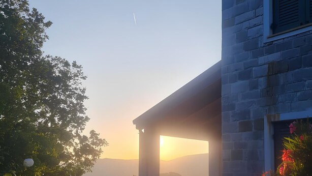 Un edificio de piedra con un espacio exterior cubierto, rodeado de follaje y flores.