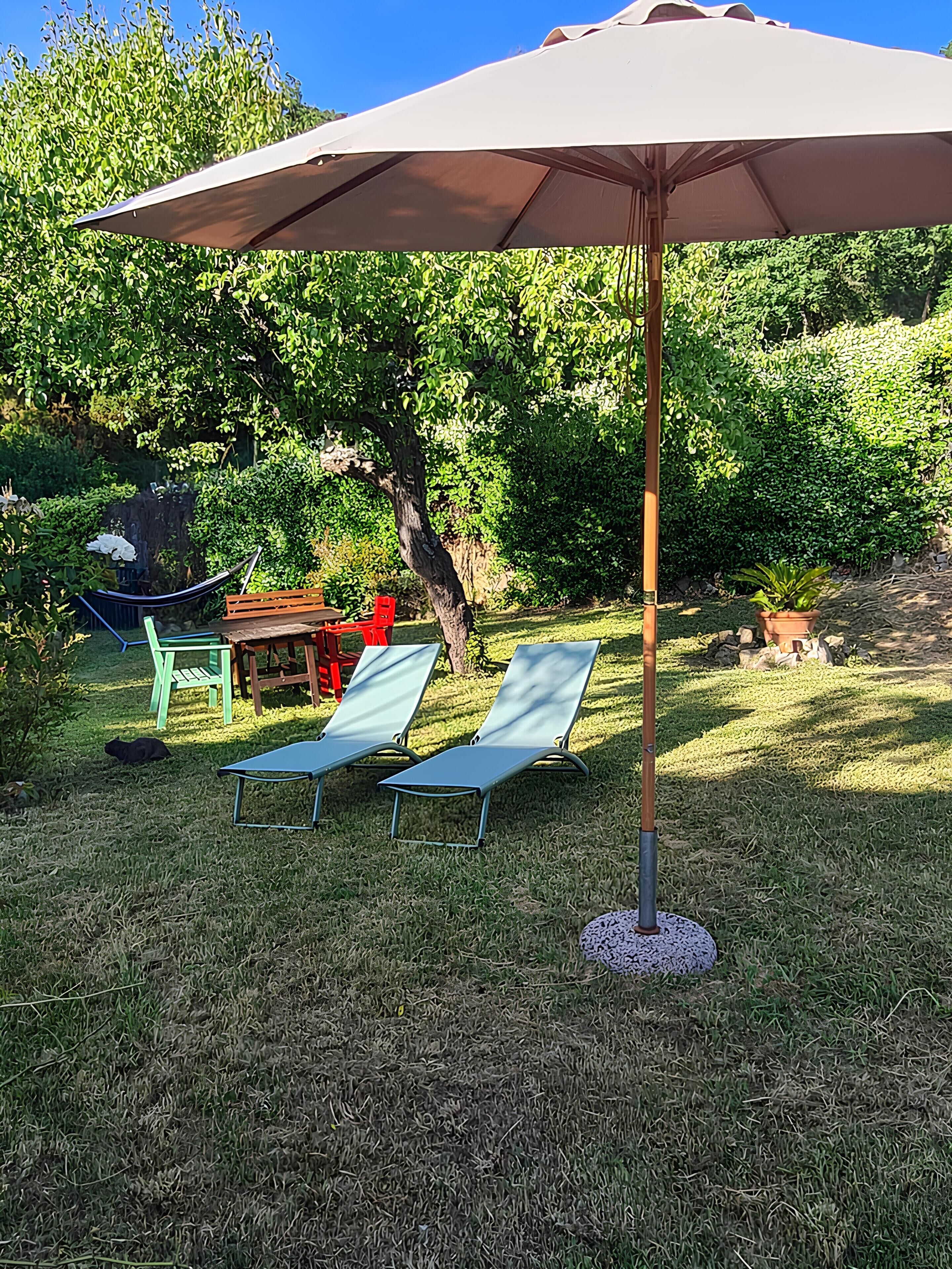 Een gazon met een buitenzitplaats, twee ligstoelen, een hangmat en een kleine tafel onder een grote parasol.