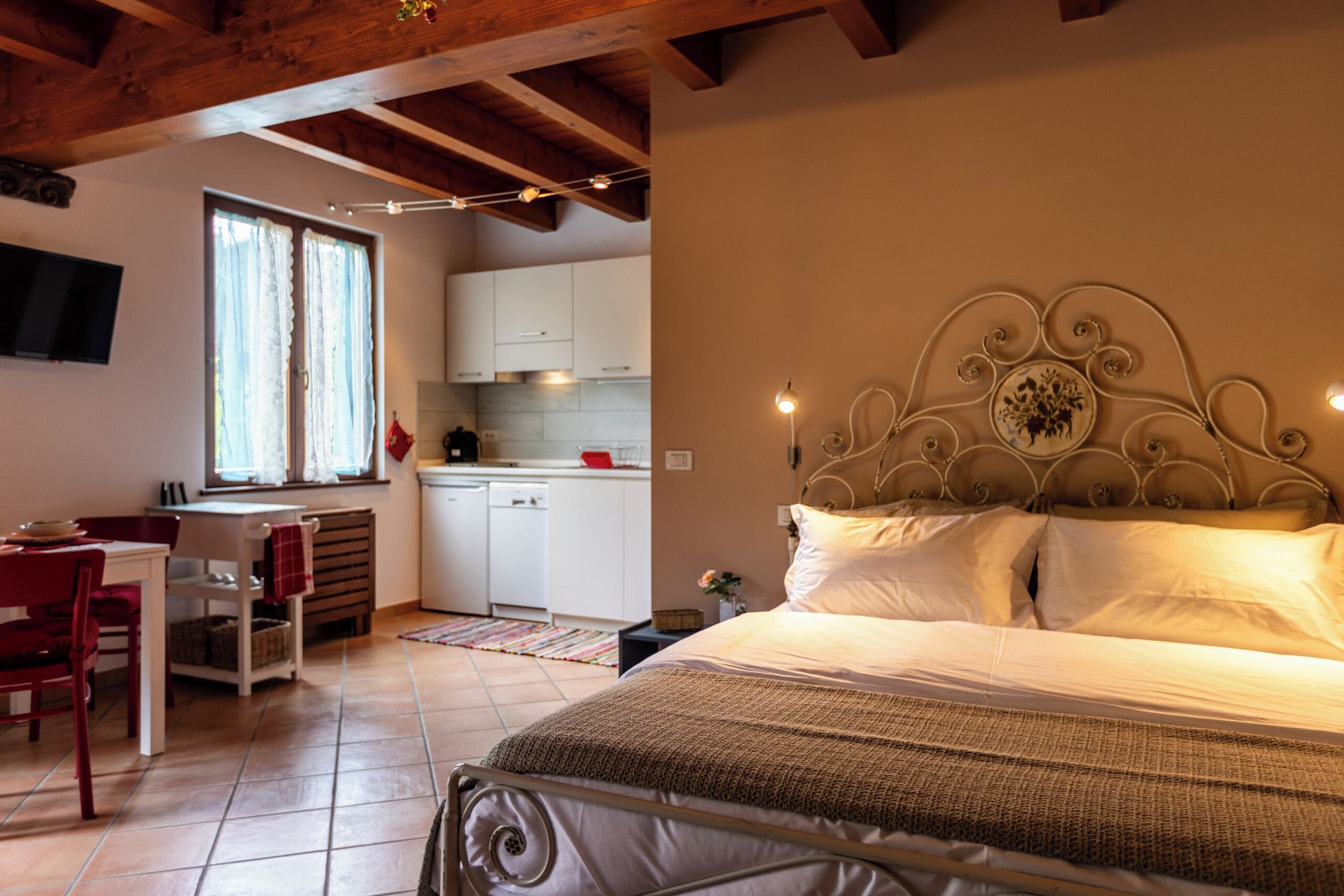 Quarto com estrutura de cama de metal, mesa de cabeceira e janela com cortinas.