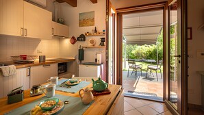Una cocina con armarios de madera, una mesa de comedor con tetera y vistas a un patio con sillas y una mesa.