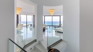 Een modern interieur met een glazen trap, een zithoek met uitzicht op de oceaan en een kroonluchter.