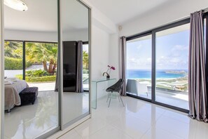 Une chambre d’hôtel moderne dotée d’une grande porte-fenêtre coulissante donnant sur un balcon avec vue sur la mer.