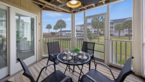 Une terrasse couverte avec une table dressée pour quatre personnes, des chaises d’extérieur et un ventilateur de plafond.