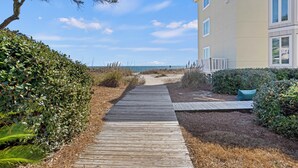 Un sentier en bois mène à un bâtiment d’où l’on a vue sur la plage.