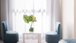 Quarto moderno com duas poltronas azuis, uma mesa branca e uma planta em vaso com folhas grandes e flores laranjas.