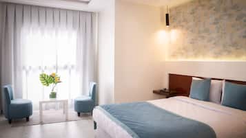 A hotel room with a large bed, two armchairs, a small table, and a potted plant.