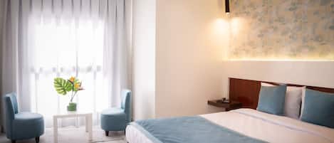 Une chambre d’hôtel avec un grand lit, deux fauteuils, une petite table et une plante en pot.