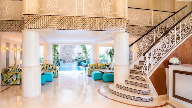 Um hall espaçoso com área de estar central, escadaria decorativa e vista para a área da piscina.