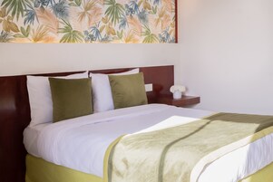 A neatly made bed with white and green bedding, a wooden headboard, and a wall with a tropical leaf pattern.