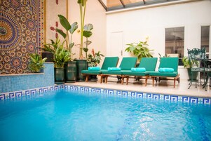 Un área de piscina con borde de baldosas, sillas de descanso y plantas en macetas.